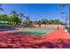 Outdoor tennis court with red and green surface, complete with lighting, fencing, and beautiful landscaping at 12335 W Rosewood Ln, Peoria, AZ 85383