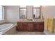 Primary bathroom featuring double sinks, a soaking tub, and wood cabinets at 16445 W Berkeley Rd, Goodyear, AZ 85395