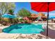 Backyard pool with mature landscaping, blue umbrellas, and a house with a basketball hoop in the background at 9137 E Odessa St, Mesa, AZ 85207