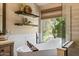 Close up of a soaking tub next to a window with view to greenery, and floating shelves at 4046 E Laurel Ave, Gilbert, AZ 85234