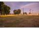 A spacious yard features lush green grass, mature trees, and a white fence under a colorful sky at 14749 E Pecos Rd, Gilbert, AZ 85295