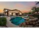 Backyard view of a pool with rock waterfall feature, surrounded by lush landscaping and patio seating at 3671 E Kingbird Pl, Chandler, AZ 85286