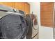Modern laundry room featuring a side-by-side washer and dryer with wood cabinets and white walls at 21483 N 65Th Ave, Glendale, AZ 85308