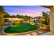 Lush backyard featuring a putting green, fire pit, covered dining area, and beautiful landscaping at dusk at 4865 S Cylinder Way, Mesa, AZ 85212