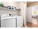 Functional laundry room with modern washer and dryer, shelving, and an open doorway at 13421 W Ocotillo Ln, Surprise, AZ 85374