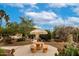 Desert backyard showcasing a tan patio table and umbrella under a bright blue sky with scattered clouds at 3700 N 149Th Ln, Goodyear, AZ 85395