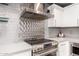 Close-up of a kitchen range, backsplash, stainless steel vent and white cabinets and countertops at 706 E Washington St # 207, Phoenix, AZ 85034