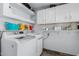 Bright laundry room with white washer and dryer, shelving, and upper cabinets at 7235 W Flower St, Phoenix, AZ 85033