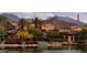 Picturesque lake view with lush landscaping, charming buildings, palm trees, and stunning mountain backdrop at 16781 S 181St Ln, Goodyear, AZ 85338