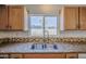 A close up of a stainless steel sink with a granite countertop and wood cabinets under a bright window at 646 W Grove Cir, Mesa, AZ 85210