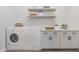 Bright laundry room with white washer and dryer, white cabinets and countertop, and open shelving at 6564 W Apex Ave, Queen Creek, AZ 85144