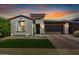 Charming single-story home at dusk with manicured lawn, stone accents, and a brick-paved driveway leading to a two-car garage at 17168 W Mountainair St, Surprise, AZ 85388
