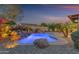 Backyard pool illuminated with underwater lights and a stone waterfall feature at twilight at 15716 W Sheridan St, Goodyear, AZ 85395