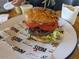 Delicious burger featuring fresh tomatoes, lettuce, and a sesame seed bun, presented on branded paper at 3653 E Highland Ave, Phoenix, AZ 85018