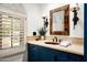 Charming bathroom with a custom vanity, stone countertop, and a decorative mirror by a shuttered window at 6019 N 62Nd Pl, Paradise Valley, AZ 85253