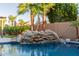 Close-up of a rock waterfall feature flowing into a sparkling pool, surrounded by lush palm trees at 9369 W Via Montoya Dr, Peoria, AZ 85383