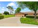 Single-story home featuring an attached two-car garage, manicured lawn and mature trees under a sunny sky at 19053 N Lakeforest Dr, Sun City, AZ 85373