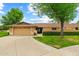 Single-story home featuring an attached two-car garage, manicured lawn and mature trees under a sunny sky at 19053 N Lakeforest Dr, Sun City, AZ 85373