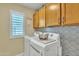 Well-lit laundry room with white machines, decorative backsplash, and wooden cabinets providing ample storage at 4545 E Wescott Dr, Phoenix, AZ 85050