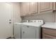 Laundry room boasts a side-by-side washer and dryer, overhead cabinets, and a door at 1350 E Vaughn Ave, Gilbert, AZ 85234
