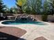 Backyard pool with rock waterfall feature, surrounded by desert landscaping, hot tub, and string lights at 4130 E Megan St, Gilbert, AZ 85295