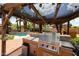 Outdoor kitchen featuring a built-in barbecue, seating, and a pool view under a wooden pergola at 4441 E Sunnyside Ln, Phoenix, AZ 85032