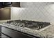 Close up of the stainless steel gas cooktop with granite countertops and white patterned backsplash at 2354 E Lieber Pl, Phoenix, AZ 85024