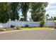 An entrance to the Hillcrest private adult community is defined by a white brick wall and lush trees and landscaping at 6 E Piping Rock Rd, Phoenix, AZ 85022