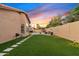 Spacious backyard featuring lush artificial turf, stone pavers, mature trees, with a sunset sky at 3295 S Ambrosia Dr, Chandler, AZ 85248