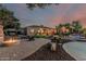 A house with a fire pit, landscaped yard, pool, and outdoor dining under a colorful sunset sky at 3754 E Flintlock Dr, Queen Creek, AZ 85142