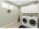 A bright laundry room featuring a front-load washer and dryer, overhead cabinets, and a window at 41769 W Canasta Ln, Maricopa, AZ 85138
