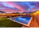 Inviting pool and spa surrounded by green grass, string lights, and desert landscaping at twilight at 5228 S 106Th Pl, Mesa, AZ 85212