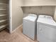 Functional laundry room with washer, dryer, storage shelves, and tiled flooring at 15369 W Wethersfield Rd, Surprise, AZ 85379