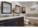 Bathroom featuring dual sinks with dark cabinets, framed mirrors, and a soaking tub with tile surround at 18802 N 71St Ln, Glendale, AZ 85308