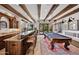 Open-concept game room featuring a pool table, bar area, exposed beams, and outdoor access at 10182 E Gilded Perch Dr, Scottsdale, AZ 85255