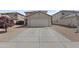 Front view of a two-car garage with wide driveway surrounded by desert landscaping with a young tree at 11915 W Charter Oak Rd, El Mirage, AZ 85335
