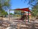 Community playground with a covered play structure, swings, and walking path surrounded by lush greenery at 36875 W Santa Maria St St, Maricopa, AZ 85138