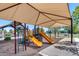 Community playground featuring a covered play structure with slides and climbing equipment in a sand-filled area at 42180 W Cheyenne Dr, Maricopa, AZ 85138