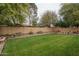 Well-maintained backyard with a lush lawn, mature trees, and flower-filled pots surrounding the patio at 15140 W Glenrosa Ave, Goodyear, AZ 85395
