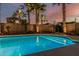 A serene pool is illuminated at night, surrounded by mature palm trees and desert landscaping, under a twilight sky at 13446 S 186Th Ave, Goodyear, AZ 85338