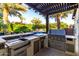 A well-equipped outdoor kitchen features a sink, stainless grill, and ample counter space, all under a pergola by mature trees at 2139 S Granite St, Gilbert, AZ 85295