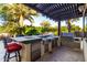 Outdoor kitchen featuring a sink, stainless grill, and counterspace, all set beneath a covered pergola with views of the pool at 2139 S Granite St, Gilbert, AZ 85295