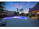 Backyard with a pool illuminated with blue lights, surrounded by mature palm trees, and patio area for entertaining at 29966 N 72Nd Dr, Peoria, AZ 85383