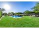Spacious backyard featuring a pool with water feature, a cozy fire pit, and lush green landscaping under a sunny sky at 17690 E Bronco Dr, Queen Creek, AZ 85142