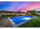 Inviting backyard pool with stone waterfall feature and well-manicured lawn in the evening at 17690 E Bronco Dr, Queen Creek, AZ 85142