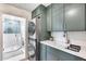 Well-organized laundry area featuring a stacked washer/dryer, sink, quartz countertop, and blue-green cabinetry at 8117 E Lewis Ave, Scottsdale, AZ 85257