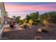 Spacious backyard featuring a rock water feature, fire pit, and desert landscaping, beautifully illuminated at dusk at 12780 W Desert Vista Trl, Peoria, AZ 85383