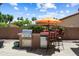 Outdoor kitchen with stainless steel BBQ, granite counter, mini-refrigerator and bar seating on a concrete patio at 3797 N 156Th N Dr, Goodyear, AZ 85395