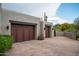 Exterior view of garage featuring wooden doors, stucco walls, desert landscaping, and brick driveway at 39847 N 105Th Pl, Scottsdale, AZ 85262