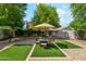Lush backyard with manicured artificial grass, rock landscaping, mature trees, and a charming patio area at 13088 N 91St Dr, Peoria, AZ 85381